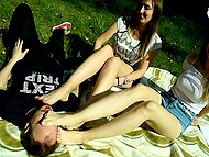 Two girls remove their shoes and offer their bare feet to a stranger man, who worships their soles in the park